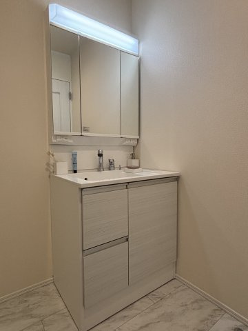 多機能で使いやすい三面鏡付きの洗面台。シャワーヘッド付きで、忙しい朝の身支度もスムーズです 。洗面室には床下収納も備わっており、日用品をスッキリと整理整頓できる機能的な設計です 。