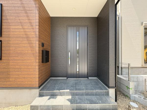 大字鴛野1期1号棟の玄関|玄関はモダンなデザインでシンプルな美観が印象的です。玄関ポーチが広く段差も低めなので、出入りしやすい造りになっています。タイル仕上げのスペースは清掃も簡単で日々のお手入れがしやすい仕様です。