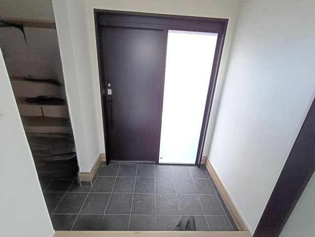 西条市小松町新屋敷甲　中古戸建の玄関|ベビーカーや趣味の道具もスムーズに搬入できる、ゆったりとした玄関スペース。モダンなタイルと照明が、住む人のセンスを感じさせます。毎日使う場所だからこそ、開放感と使いやすさを追求した設計が光ります。