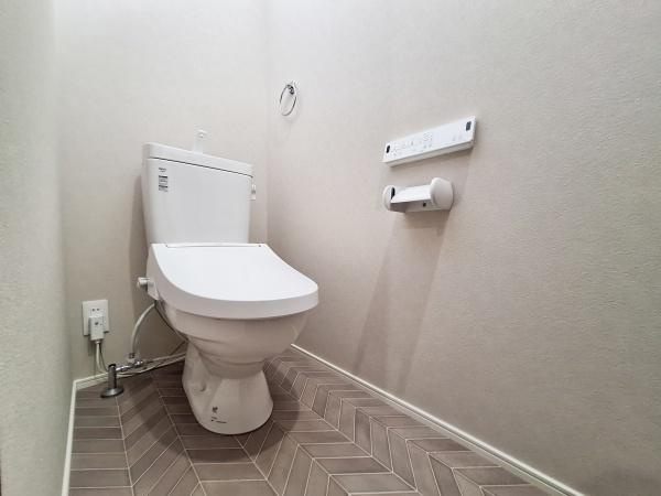 AG-HOUSE　梅が丘　A棟のトイレ|清潔感のあるトイレ空間です。シンプルなデザインで落ち着いた雰囲気が漂います。床のヘリンボーン柄が特徴的です。使い勝手の良いペーパーホルダーやリモコンも設置されています。壁面や設備も整っています。