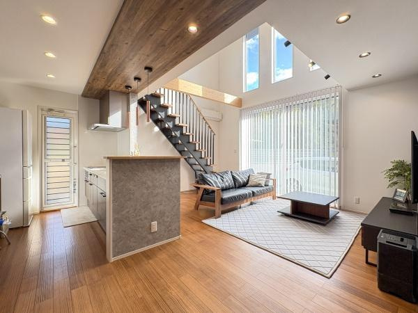 角子原　戸建ての居間・リビング|大きな窓から自然光が差し込む明るいリビングです。天井が高く開放感のある空間となっています。スタイリッシュなデザインの階段が特徴的です。木目調の床が落ち着いた雰囲気を演出しています。