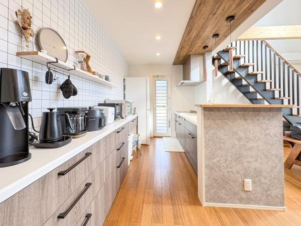 角子原　戸建ての居間・リビング|木目調のフローリングと白い壁が明るい空間を演出しています。キッチンカウンターとリビングが一体になっており開放感があります。階段横の造作も印象的で室内全体が統一感のあるデザインです。