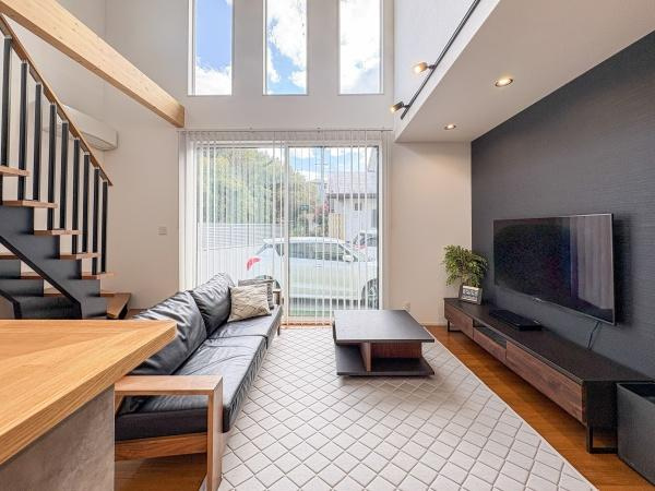 角子原　戸建ての居間・リビング|吹き抜けの大きな窓からたっぷりと自然光が入ります。落ち着いた色合いの壁面とモダンなデザインの階段が印象的です。家具がスマートに配置されており空間にゆとりがあります。