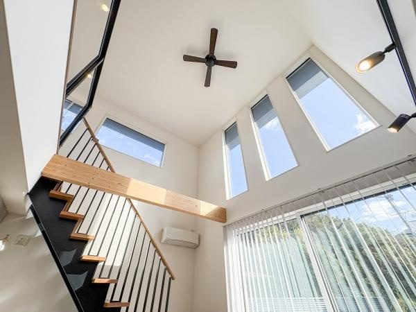 角子原　戸建ての居間・リビング|吹き抜けの天井が開放感を演出しています。大きな窓から明るい陽射しが差し込みます。スタイリッシュな階段デザインが特徴です。天井のシーリングファンが空間を引き締めています。モダンな雰囲気が魅力的です。