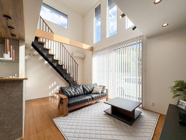 角子原　戸建ての居間・リビング|吹き抜けのリビングが明るい雰囲気を演出しています。大きな窓から自然光がたっぷりと差し込みます。木目調の床やシンプルなインテリアが空間を引き立てます。階段もスタイリッシュなデザインです。