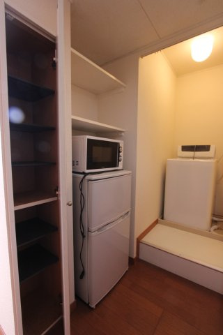 プチ・フルールのその他|【家具家電付き】キッチン通路にはレンジ、冷蔵庫、洗濯機の家電付き（残物）　また、左手前に見えるのは靴箱に使える収納です。棚の高さが変えられるため、ブーツなども収納できます。