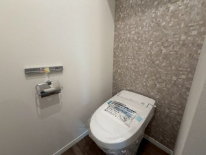 【トイレ】 | デザイン性の高いアクセントクロスが施された落ち着きあるトイレ空間。温水洗浄便座などの快適設備を備え、手洗い器も付いているため毎日の利用がより衛生的でスマートに行えます！