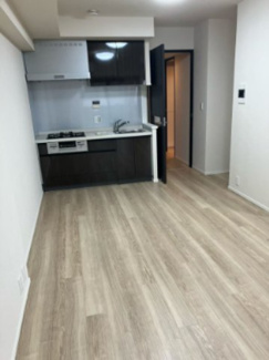 【居間・リビング】 | シティタワー銀座東 | 明るい木目調のフローリングが印象的なリビングです。窓からは東向きの柔らかな光が差し込み、開放感も抜群。シックなカラーのシステムキッチンが空間を引き締め、洗練された都心ライフを演出します。