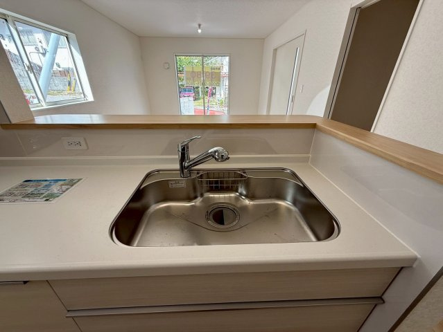 クレイドルガーデン那覇市識名 第３・１号棟のキッチン|浄水器付きキッチンの流し台／リビングの眺め