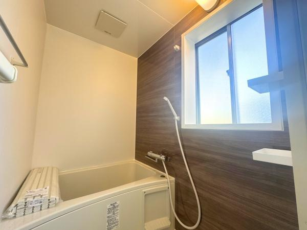 大字横尾　中古の浴室|明るい窓付きのバスルームです。清潔感のある内装とアクセントパネルが特徴です。浴槽には便利なふたも備わっています。換気設備が整っており湿気対策も安心です。収納スペースもしっかり確保されています。