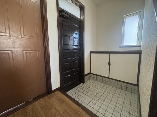 大字横尾　中古の玄関|玄関には収納スペースがしっかり確保されています。明るい窓があるため玄関全体が爽やかに感じられます。使い勝手の良いタイル張りでお手入れも簡単です。木目調のドアが落ち着いた雰囲気を演出します。