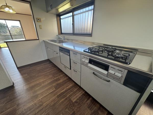 大字常行　中古のキッチン|窓からの自然光が差し込むキッチンは明るく開放的な雰囲気です。シンプルなデザインのシンクとコンロが配置され調理スペースも確保されています。床材は落ち着いたトーンで清潔感のある印象です。