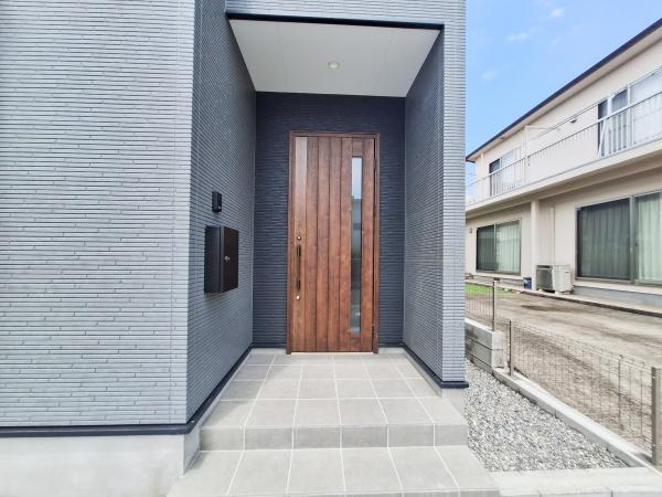 宗方台西1期2号棟の玄関|シンプルで落ち着いた外観デザインの玄関が特徴です。木目調のドアがアクセントになっており全体的に統一感があります。玄関ポーチも広めでゆとりを感じられる仕様です。モダンな印象を与える玄関です。