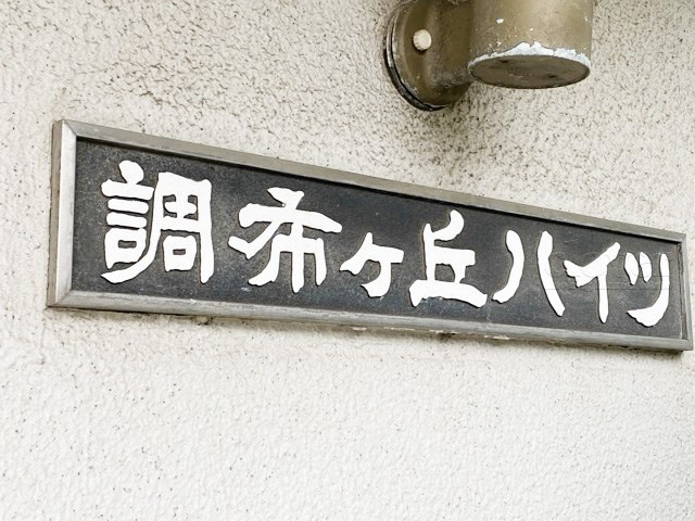 【現況写真】 | 調布ヶ丘ハイツ | エントランスに掲げられた、マンション名を示す館銘板。さほど激しく主張はしませんが、しっかりと掲示されています。～即日のご見学可能～　お問合せはお気軽にどうぞ。