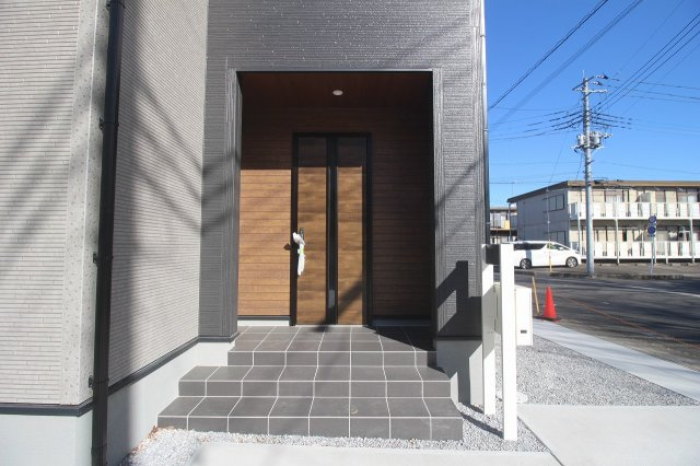 下野市緑2丁目　第2の玄関|木目調の玄関ドアが印象的な玄関アプローチ。屋根付きで雨の日も出入りしやすく、落ち着いた雰囲気が住まいの第一印象を引き立てます。