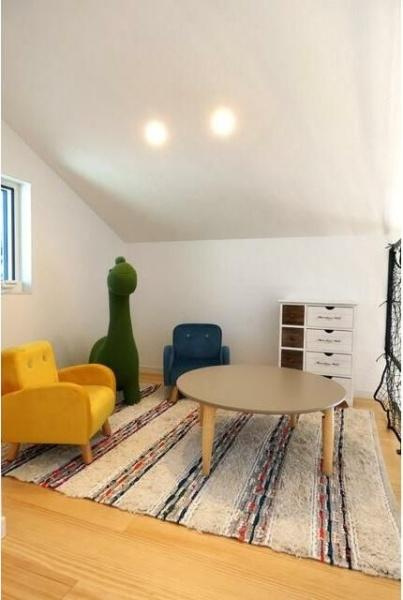 HT久原4号地の内装|斜め天井が印象的な空間です。カラフルな椅子や遊び心のあるインテリアが配置されています。明るい色合いの床やラグがアクセントになっています。窓から自然光が差し込み開放的な雰囲気です。
