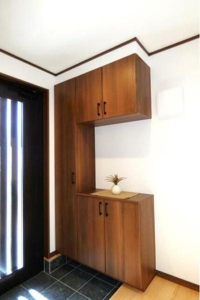 HT久原4号地の玄関|木目調の収納が印象的な玄関です。明るい色合いで空間がすっきりとまとまっています。収納力のある構造で日々の使い勝手も良好です。シンプルなデザインで幅広いインテリアに合わせやすい点が魅力です。