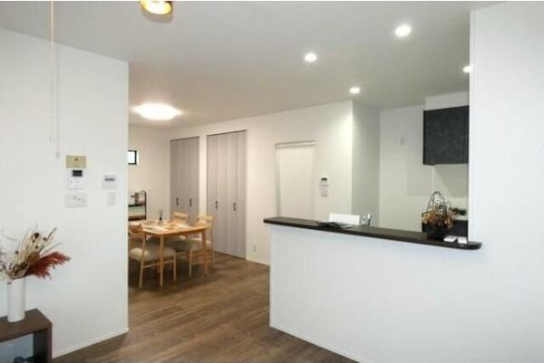 HT久原2号地の居間・リビング|白を基調とした明るいリビングです。天井にはダウンライトが配され空間全体にやさしい光が行き渡ります。キッチンカウンター越しにダイニングスペースが広がり使い勝手の良いレイアウトです。