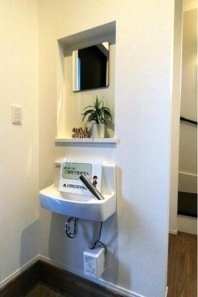 HT久原2号地の玄関|玄関にコンパクトな手洗いスペースが設置されています。鏡と小物を飾れる棚があり空間をすっきりと見せています。帰宅後すぐに手洗いができる配置がポイントです。ホワイトを基調としたデザインで清潔感があります。
