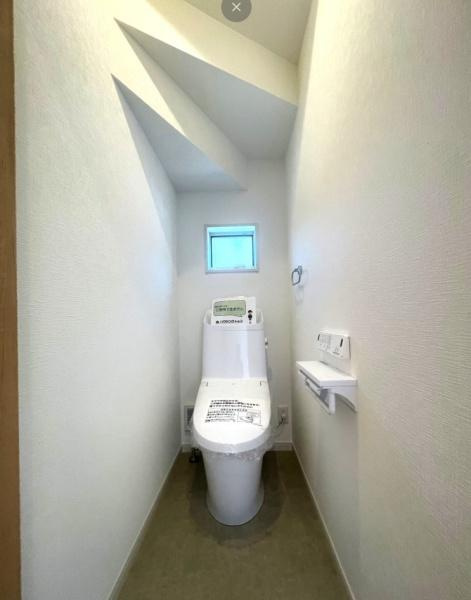 HT久原1号地のトイレ|小窓から自然光が入り明るい印象のトイレです。シンプルなデザインで清潔感があります。天井の形状も特徴的で空間にアクセントを加えています。壁リモコンの設置で使い勝手にも配慮されています。