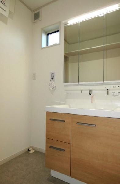 HT久原1号地の独立洗面台|清潔感のある洗面台は木目調の収納が特徴的です。鏡裏にも収納スペースがありすっきりとした印象です。小窓から自然光が入りやすく明るい空間となっています。