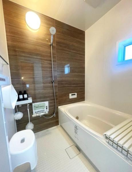 HT久原1号地の浴室|木目調のアクセントパネルが印象的なバスルームです。大きな浴槽でゆったり過ごせます。明るい照明と換気窓があり清潔感のある空間です。使いやすいシャワー設備も整っています。