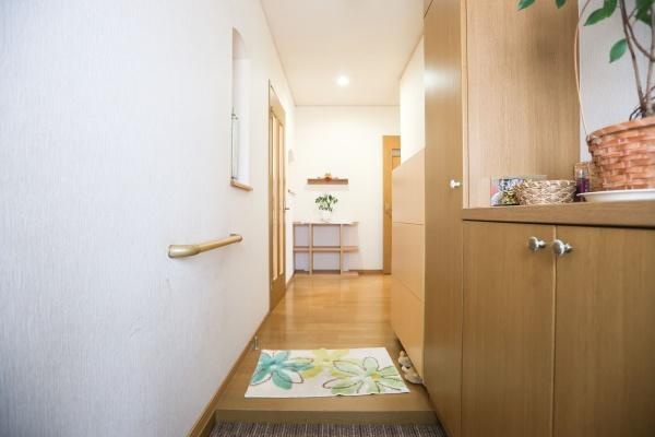城東町　戸建ての玄関|木目調の収納が玄関に温かみを与えています。手すりが設置されているので安心して利用できます。フラットな床面が歩きやすさをサポートします。奥には飾り棚があり空間にアクセントを加えています。