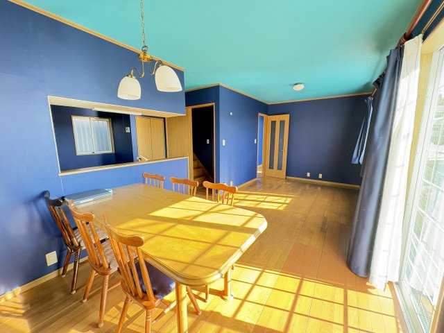 売中古戸建　清水町伏見の居間・リビング|落ち着きのあるネイビーカラーの壁と、温かみのあるフローリングが調和し、シンプルながらも洗練された雰囲気です。家具配置もしやすい間取りで、ダイニングとくつろぎ空間をゆったり分けて使えます。