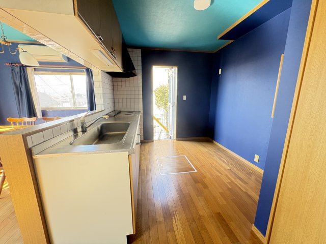 売中古戸建　清水町伏見のキッチン|深みのあるブルーのアクセントクロスが空間を引き締め、木目調のフローリングとのコントラストが映える、デザイン性の高い内装です。掃き出し窓からは自然光が入り、日中は明るく心地よい空間が広がります。