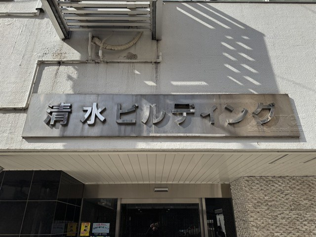 【現況写真】 | 清水ビル | エントランスに掲げられた、マンション名を示す館銘板。さほど激しく主張はしませんが、しっかりと掲示されています。～即日のご見学可能～　お問合せはお気軽にどうぞ。

