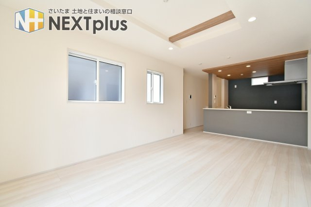 白岡市小久喜4期の居間・リビング|折上天井と木目調の梁が、縦の広がりと洗練された贅沢感を演出。グレーのキッチン腰壁が空間のアクセントになり、モダンで落ち着いたリビングライフを叶えます。家族が自然と集まりたくなる、開放感に満ちた住まい。