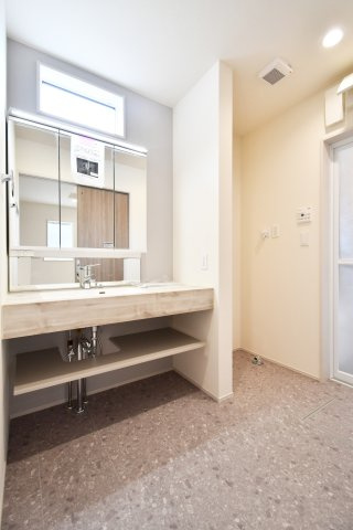 白岡市小久喜4期の独立洗面台|まるでホテルのような洗練されたデザイン。ワイドな三面鏡とカウンターが、忙しい朝にゆとりを与えます。下部のオープン収納は、タオルやお洒落なバスケットを置くのにおすすめ。高窓からの光が明るく包み込みます。