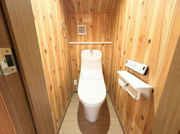 角子原二丁目　戸建てのトイレ|温かみのある木目調の壁が特徴的なトイレです。白を基調とした設備が清潔感を演出しています。収納やリモコンも使いやすい位置に配置されています。