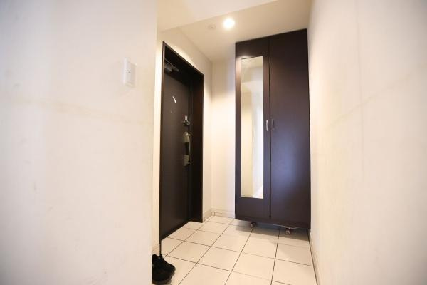 ラグジン高松西の玄関|玄関には大きな収納が設置されており整理整頓がしやすい空間です。タイル張りの床が清潔感を演出しています。ダークカラーのドアと収納が印象的な雰囲気を加えています。全体的にすっきりとした印象の玄関です。