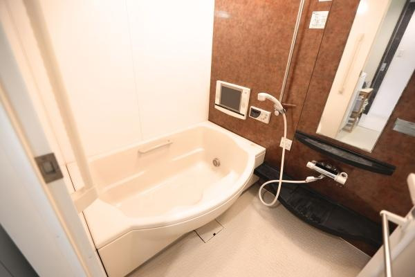 ラグジン高松西の浴室|浴室内にテレビがありゆったりとしたバスタブが特徴です。壁面の落ち着いた色合いが空間にアクセントを与えています。大型ミラーが設置されており開放感があります。収納棚もあり使い勝手が考えられています。