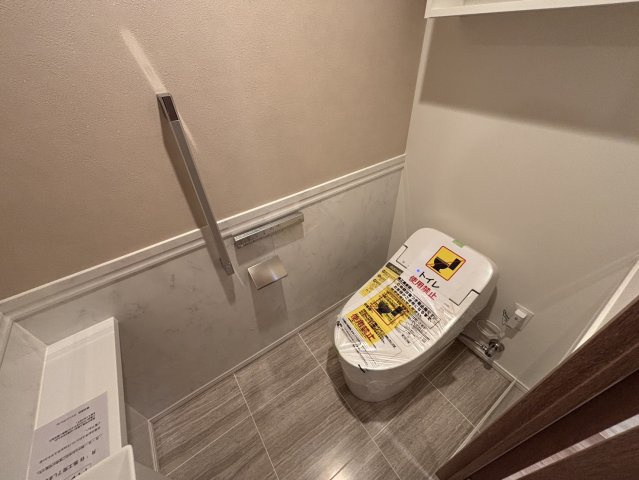 【清潔感溢れるトイレ】手洗いカウンター付きのタンクレストイレを採用し、スッキリとした空間に。上部には収納棚も完備しています。落ち着いた色調の内装が、プライベートな時間に安らぎを与えてくれます。