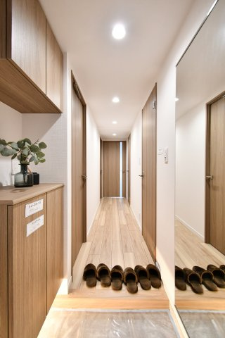 ライオンズマンション大宮浅間町の玄関|温かみのある木目調の建具とフローリングが、リフォームによる新生活の始まりを予感させます。廊下にはダウンライトを贅沢に配置し、奥行きのある明るい空間を演出。随所のこだわりが光ります。