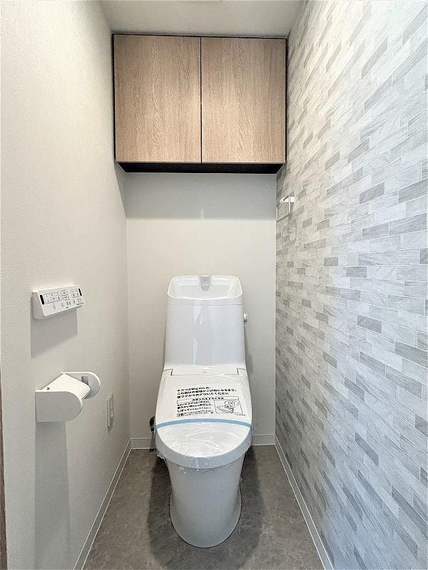 カサーレ小平のトイレ|温水洗浄便座機能付きのトイレです。上部には吊戸棚もございますので、トイレ用洗剤やトイレットペーパーの収納に便利です。また、今回のリフォーム工事で一部アクセントクロスに変更をしております。