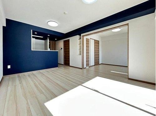 サンクレイドル武蔵野鷹の台の居間・リビング|ネイビーのアクセントクロスが洗練されたモダンな印象を与えます。隣接する洋室の扉を開放することで、リビングをより広く、奥行きのある大空間として活用いただけます