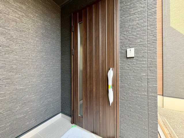 「続き間で23帖超えの大空間」香美市土佐山田町東本町2号棟　新築一戸建ての玄関|重厚感のある木目調のデザインが印象的な玄関ドア。黒い外壁とのコントラストが美しく、家の顔として洗練された雰囲気を演出します。