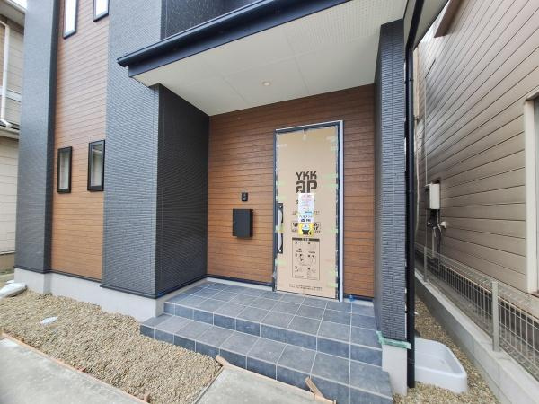 今津留2丁目1期1号棟の玄関|玄関周りは落ち着いた色合いで統一されており住まい全体に調和を感じます。広めのステップが設けられており段差の昇り降りも安心です。外観のアクセントとして木目調の壁面が使用されています。