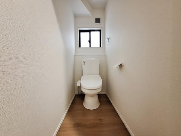 今津留2丁目1期1号棟のトイレ|シンプルなデザインで清潔感のあるトイレです。窓があるため換気もしやすく明るい雰囲気が保たれます。壁紙や床の落ち着いた色合いが空間を引き締めています。ペーパーホルダーも設置されています。