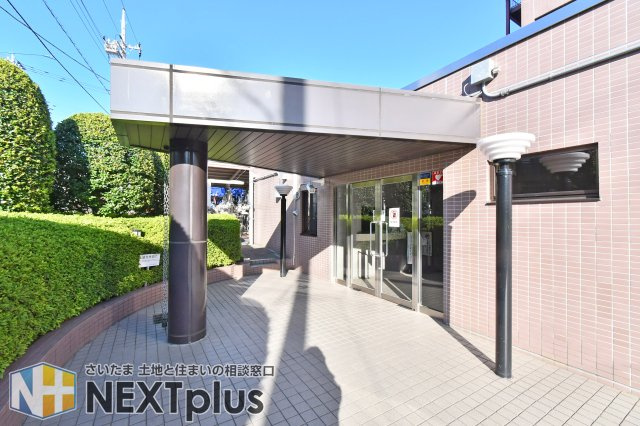 ファミール大宮宮原壱番館|【エントランス（外）】庇付きのアプローチで雨の日も出入りしやすい造り。植栽のある共用部で、建物入口の雰囲気を写真で確認できます。夜間の明るさ・段差・雨天時の滑りやすさは内覧で要確認です。