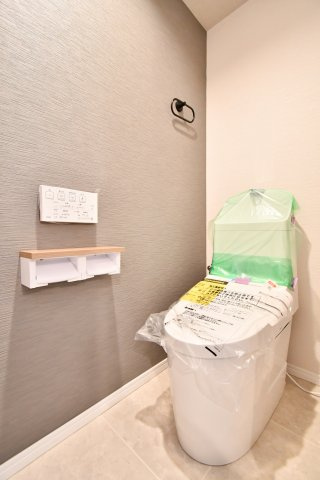 ライオンズプラザ大宮のトイレ|グレーのアクセントクロスが映えるトイレ。棚付きでペーパーや掃除用品を置きやすく、操作パネルも手の届く位置。床と壁がシンプルなので圧迫感が出にくく、お手入れもしやすい空間です。動作もしやすい広さ。
