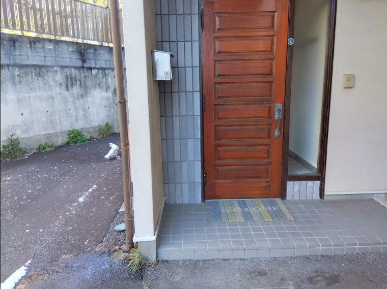 売中古戸建　三島市若松町の玄関|温かみのある木目調の玄関ドアが印象的なエントランスです。
屋根付きのポーチ仕様となっており、雨の日でも落ち着いて鍵の開閉が可能です。タイル張りの玄関まわりはお手入れもしやすく、清潔感を保てます。
