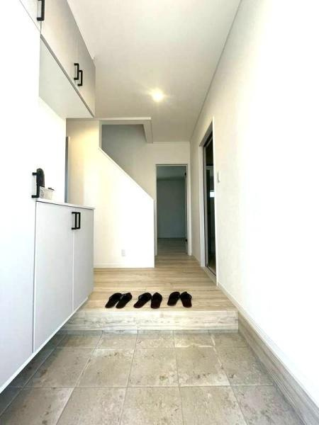 HT挾間の玄関|白を基調とした玄関が明るくすっきりとした雰囲気を演出しています。収納スペースが充実しており整理整頓も容易です。段差のある設計が空間にメリハリを与えています。床材と壁の質感が調和し清潔感を感じさせます。