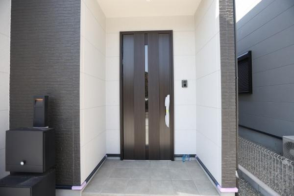 P-TELAS牧１丁目3号地の玄関|玄関は落ち着いた色調で統一されシンプルながらも存在感のある扉が出迎えます。明るいタイルが空間を清潔に見せています。外壁とのコントラストもバランス良く配置されています。