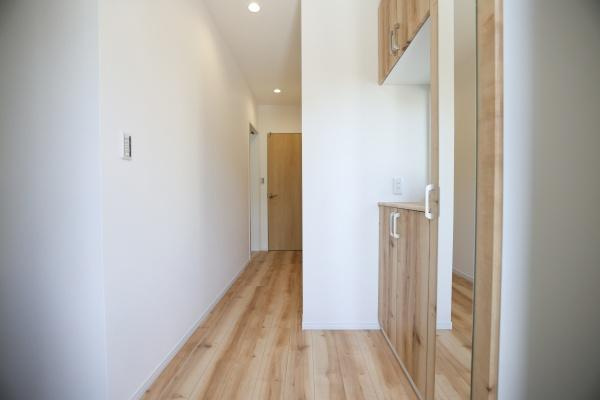 P-TELAS牧１丁目2号地の玄関|木目調の収納が印象的な玄関です。白を基調とした壁と天井で空間がすっきりとしています。照明の配置も工夫されており明るい印象を与えます。床材と収納の色合いが統一されており落ち着いた雰囲気です。