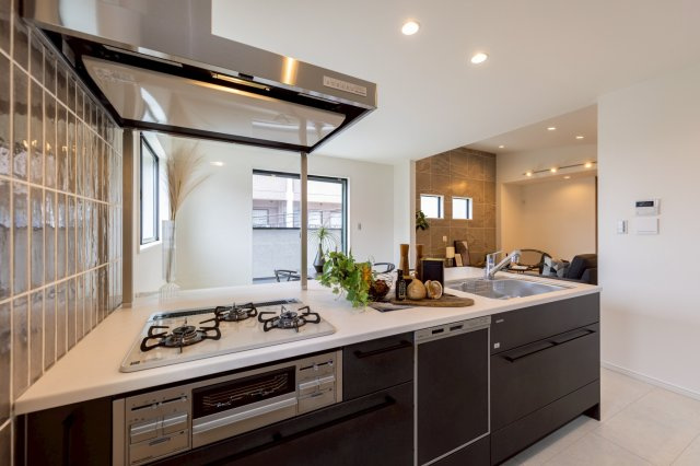 神戸市灘区高尾通1丁目新築一戸建て│3LDK+駐車2台可(車種制限有)のキッチン|キッチンを収納庫奥側から撮影した内観写真です。コンロ前は視界を確保した耐熱パネル使用。コンロはもちろんガラストップ施工で掃除がらくらく！整流板もフラットタイプでスタイリッシュな印象を確保しました。