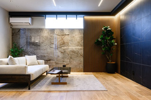 【居間・リビング】 | リビングの壁面には表情豊かな大判タイルを採用。間接照明の柔らかな光が壁の凹凸を際立たせ、落ち着いた夜の時間を彩ります。お気に入りのソファに身を委ね、ゆったりと映画鑑賞や読書を楽しむ贅沢な日常を。